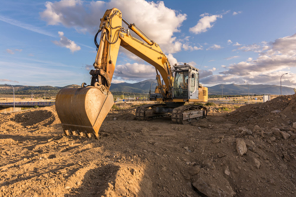 Maquinaria excavadora trabajando en un campo de terracería rodeado de montañas